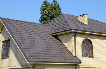 House of yellow brick and brown corrugated roof made of metal. Lattices on the windows.
