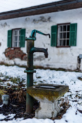 faucet in the snow in front of an old farmhouse