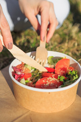 concept takeaway dishes, fresh salad greens, tomatoes and sprouted grains in paper plate in the hands of a young girl who eats it outdoors