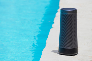 Modern portable music speaker with voice assistant near the swimming pool.