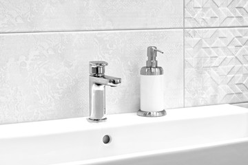 Luxury modern style faucet mixer and liquid soap on a white sink in a beautiful gray and white...