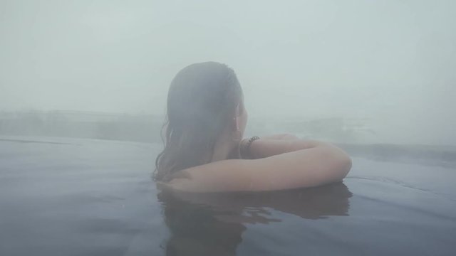 Back view of young girl in open hot thermal swimming pool. Traveling Pretty young lady relaxing in mountains valley. Enjoy in pool at Winter day