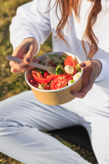 concept takeaway dishes, fresh salad greens, tomatoes and sprouted grains in paper plate in the hands of a young girl who eats it outdoors