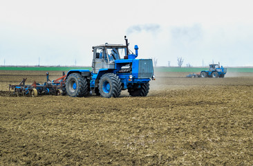 Obraz premium Lush and loosen the soil on the field before sowing. The tractor plows a field with a plow