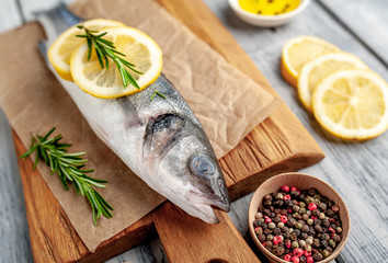 chilled raw sea bass fish with ingredients on a cutting board on a wood background