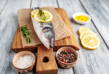 chilled raw sea bass fish with ingredients on a cutting board on a wood background