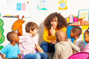 Teacher in kindergarten  reading a book to kids