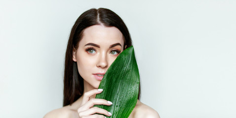 Portrait of young beautiful woman with healthy glow perfect smooth skin holds green tropical leaf. Organic, natural cosmetics, skincare, wellness, beauty clinic, facial treatment, cosmetology concept.