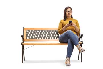 Young female sitting on a bench and typing on a mobile phone