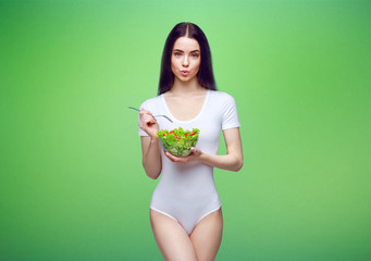 Beautiful slim brunette young girl in white lingerie on green background. Sporty healthy model holding a fresh vegetable salad bowl. Sport, diet, healthy food, nutrition, lifestyle, fat burn concept.