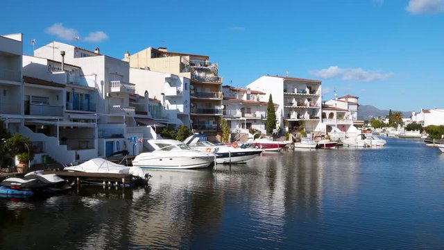 Beautiful panorama of the houses and hotels on the shores of the picturesque Mediterranean canal in the Golf de Roses against the backdrop of mountains and blue sky. Motor boats moored to the pier in 