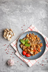 Fried oyster mushrooms with tomatoes on gray concrete background. Top view.