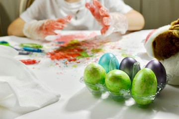 A child in painted gloves on a back blurred background and Easter colorful eggs.