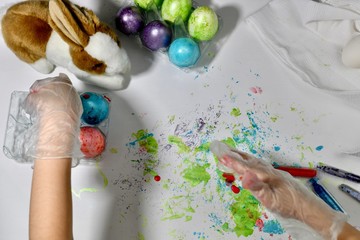 Childish hands in gloves put painted eggs in a container.