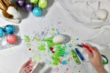 Children's hands are painting eggs in red on the working surface.
