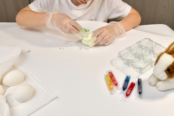 Children's hands are engaged in coloring eggs in green color on the working surface.