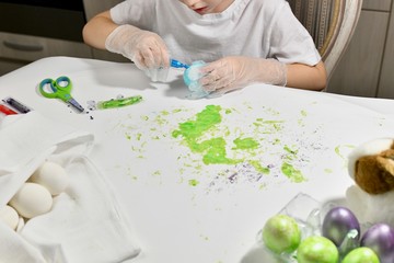 Children's hands are engaged in coloring eggs in green color on the working surface.