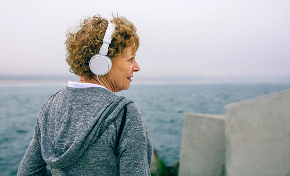 Closeup of senior sportswoman with headphones looking aside by sea pier