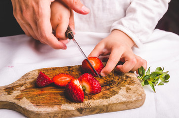 Mother helps child to slice strawberry with knife