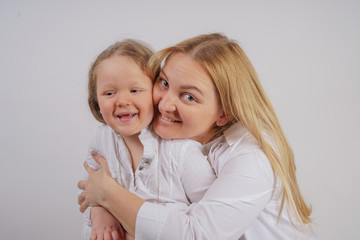 mom and daughter in white shirts with long blonde hair posing on a solid background in the Studio. charming family takes care of each other and hugs.