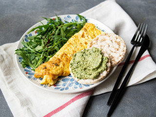 Healthy breakfast - scrambled eggs, arugula and bread with pesto on gray background. Perfect eggs omelette with fresh arugula and pesto cracker. Vegetarian food. Diet. Selective focus, close up.