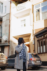 Attractive positive young girl wearing glasses in a coat on the background of buildings on cars