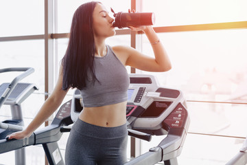 Fototapeta premium Girl in the gym are trained on treadmill and drink water