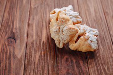 A fresh sweet pastry is sprinkled with sugar powder on a wooden background