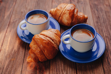 two cups of coffee and croissants on a wooden background, good light, morning atmosphere