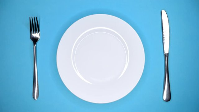 Table setting in restaurant or cafe. Fork and knife. Female hands puts and takes away white plate from blue table