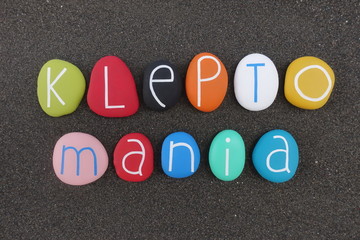 Kleptomania word composed with multi colored stones over black volcanic sand