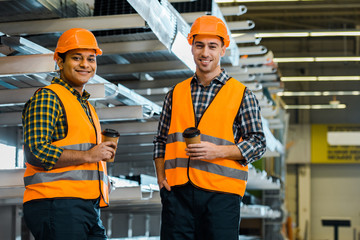 cheerful multicultural workers holding paper cups and looking at camera