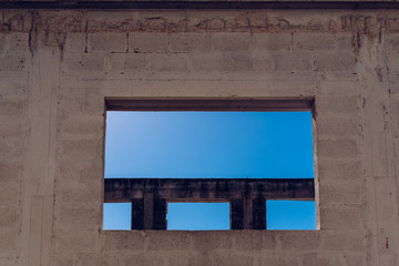 Window of abandoned building without finishing its construction, intense sun and deep blue sky background.