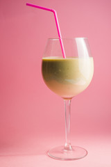 Banana and pear smoothie, on a tall elegant glass often used for wine, with pink straw against a pink background