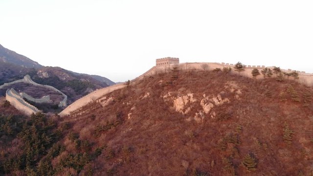 Great Wall of China following mountainous terrain, aerial shot at sunset hour. Fortification wall made from stone bricks, running on crest of hill