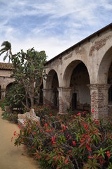 Obraz premium San Juan Capistrano, CA., U.S.A. Ap. 21, 2018. Mission courtyard, fired red brick pillared portico, fountains & water lilies, packed dirt, flat red brick-set paths, beautiful palms, trees & floral 
