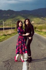 two young twins sisters in the middle of road in colorful dress with flowers