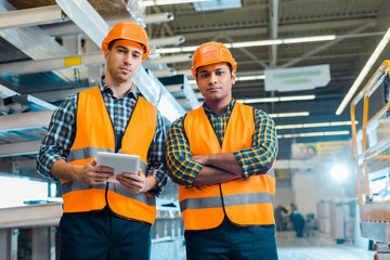 serious multicultural workers in safety vasts and helmets looking at camera