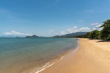 Cairns, Australia - February 18, 2019: Warm beige tropical beach of Palm Cove with azure Coral Sea water under blue sky with rainforested mountains on horizon.