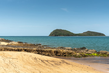 Fototapeta na wymiar Cairns, Australia - February 18, 2019: Green Double Island off Warm beige tropical beach of Palm Cove with azure Coral Sea water under blue sky..