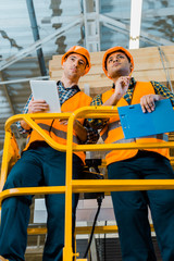 warehouse workers with digital tablet and clipboard standing on scissor lift