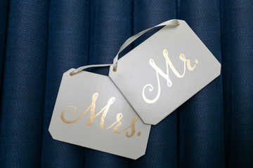White square plaques with white ribbons and Golden inscriptions Mr and Mrs isolated on blue background.