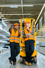 handsome indian worker pointing with hands while standing with colleague near scissor lift