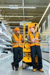 smiling multicultural workers talking while standing near scissor lift