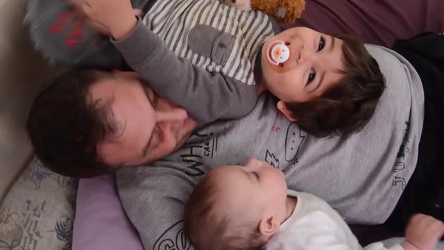 Father and two sons, baby and toddler, playing together on the bed