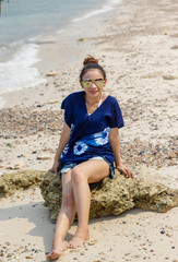 Women white skin lovely brown hair put mercury color glasses wear blue shirt wearing shorts jeans blue women sit poses photography portrait at the rocks on beach.