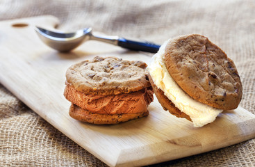Two ice cream sandwiches on a wood cutting board on a burlap background.