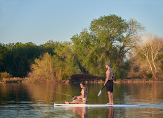 A young couple enjoying their romantic vacation by paddle boarding on a small Northern California lake on a Summer afternoon.