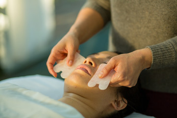 Young woman receives facial rejuvenation with gua sha rose quartz in spa wellness center