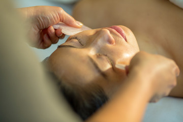 Young woman receives facial rejuvenation with gua sha rose quartz in spa wellness center